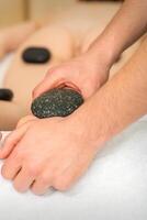 Two masseurs make a foot massage with a hot stone in four hands at the spa. photo