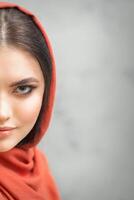 Portrait of a pretty young caucasian woman with makeup in a red headscarf on gray background. photo