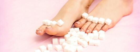 Sugar cubes lying in a row on female feet on pink background with copy space, depilation concept. photo