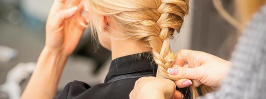 Braiding braid. Hands of female hairdresser braids long braid for a blonde woman in a hair salon. photo