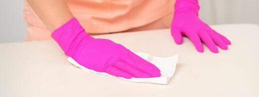 Close up of hands in rubber protective pink gloves cleaning the white surface with a white rag. photo