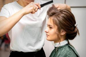 Professional hairdresser doing hairstyle for a beautiful brunette young woman with long hair. Concept of fashion and beauty. photo