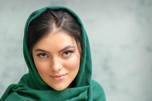 retrato de un bonito joven caucásico mujer con maquillaje en un verde Pañuelo en gris antecedentes. foto