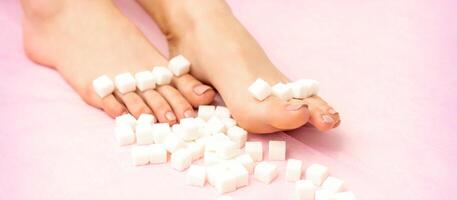 Sugar cubes lying in a row on female feet on pink background with copy space, depilation concept. photo