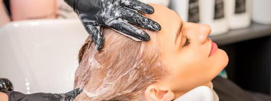 Young caucasian blonde woman having hair washed in the sink at a beauty salon. photo