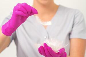 The beautician holds white feathers in her gloved hands over white background. Concept of health softness skin and body care. photo