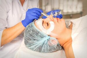 Face peeling at the beautician. Facial treatment. The beautician applies a cleansing face mask to the female patient. photo