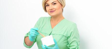 Cosmetician holding a jar of wax for depilation smiling on a white background. Natural product for hair removal. Copy space. photo