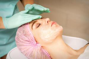 Face peeling at the beautician. Facial treatment. The beautician applies a cleansing face mask to the female patient. photo