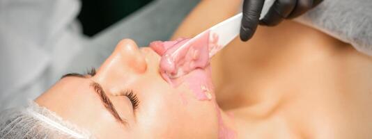 Beautician applying alginate peel-off powder facial mask with the spatula in a spa. photo