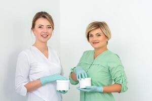 dos esteticistas con frascos de cera para depilación sonriente en contra un blanco antecedentes. natural producto para pelo eliminación. Copiar espacio. foto