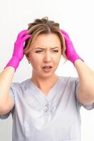 The emotionally shocked young female medical worker holding hands on her head fell into panic on white background, infection, epidemic, virus, and disease concept. photo