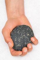 Hand of masseur holding massage stone on white background, top view. photo