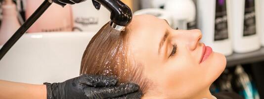 Young caucasian blonde woman having hair washed in the sink at a beauty salon. photo