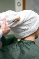 A hairdresser is wrapping the wet hair of the young woman in a towel after washing at the beauty salon. photo