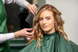 peluquero haciendo cortes de cabello para el mujer mientras peinada con cepillo para el pelo, peine en un pelo salón. foto