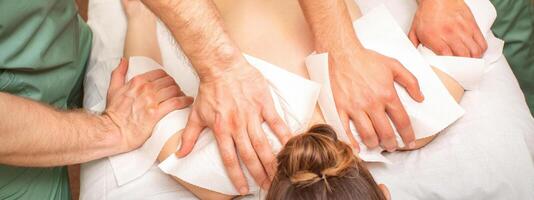 Back Massage with four hands in the spa salon. Two massage therapists make a back massage for a young woman. photo