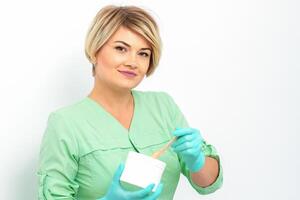 Cosmetician holding a jar of wax for depilation smiling on a white background. Natural product for hair removal. Copy space. photo