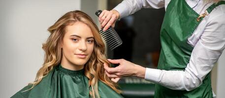 peluquero haciendo cortes de cabello para el mujer mientras peinada con cepillo para el pelo, peine en un pelo salón. foto