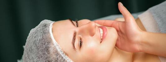 médico examinando el hermosa cara de joven sonriente mujer en belleza clínica. foto