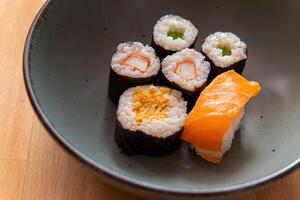 bowl of assorted sushi sits on a wooden table photo