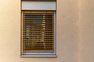 window with wooden blinds is shown against a brown wall photo