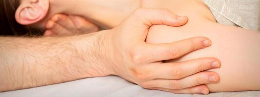 Male masseur massaging shoulder of a young woman lying on a massage table in a spa clinic. photo