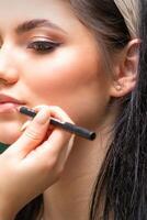 maquillaje profesional artista o cosmetóloga es pintura contorno labios de un joven mujer con un lápiz cerca arriba. foto