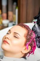 Washing dyed female hair. Professional hairdresser washes pink color paint off of a customer. Young caucasian woman having her hair washed in a beauty salon. photo