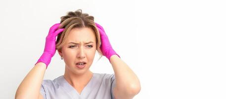 The emotionally shocked young female medical worker holding hands on her head fell into panic on white background, infection, epidemic, virus, and disease concept. photo