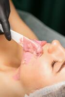 Beautician applying alginate peel-off powder facial mask with the spatula in a spa. photo