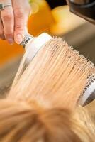 Hairdresser hand drying blond hair with a hairdryer and round brush in a beauty salon. photo