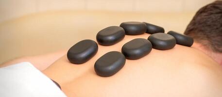 Hot stone massage therapy. Caucasian young man getting a hot stone massage on back at spa salon. photo