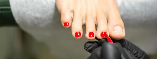 pedicuro aplicando rojo uña polaco a el hembra uñas de los pies en un belleza salón. foto