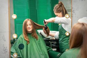 peluquero haciendo cortes de cabello para el mujer mientras peinada con cepillo para el pelo, peine en un pelo salón. foto