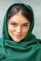 Portrait of a pretty young caucasian woman with makeup in a green headscarf on gray background. photo