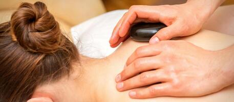 Hot stone massage therapy. Caucasian young woman getting a hot stone massage on back at spa salon. photo