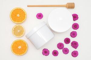 Flat lay composition of white jars with orange slices and flowers on white background, skincare cosmetics, top view. photo