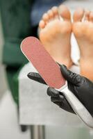 Special grater for scrubbing heels in hands of nail pedicure technician on feet background in beauty salon closeup. photo