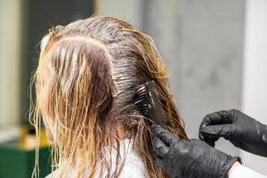 A hairdresser in black gloves is applying brush color to the hair of a customer. Hair coloring in a beauty salon close-up. photo