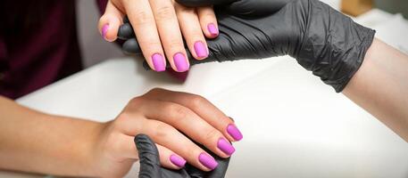 Examination of manicured fingernails. Hands of manicure master in black gloves examining female pink nails in manicure salon. photo