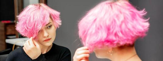 hermosa joven caucásico mujer mirando a su corto rosado pelo en un espejo. foto