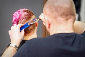 mujer teniendo un nuevo Corte de pelo. masculino estilista corte rosado corto pelo con tijeras en un pelo salón. foto