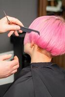 Hands of hairdresser combing hair making short pink hairstyle for a young caucasian woman in a beauty salon. photo