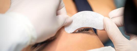 The beautician is gluing a patch under her eyes, before the procedure of eyelash extension. Artificial extended eyelashes. photo