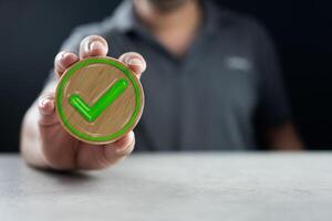 Man shows a wooden circle block with a check mark icon. Vote and choose correct photo