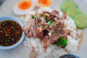 Braised pork placed on hot steamed rice served with boiled egg and sliced cucumber photo