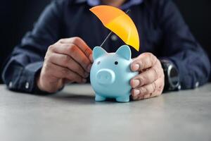 Man sheltering piggy bank with umbrella. Risk insurance in banking photo