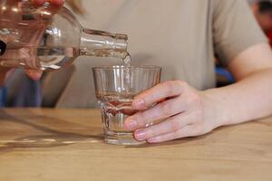 Hand pouring water from bottle into glass at wooden table photo