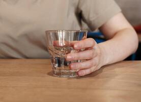 mano tenencia, tomando agua vaso a de madera mesa foto